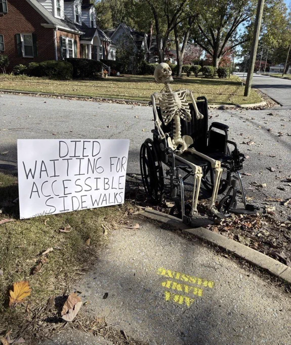 A skeleton sitting on a wheelchair beside a curb and assign beside it saying: died waiting for Accessible sidewalk