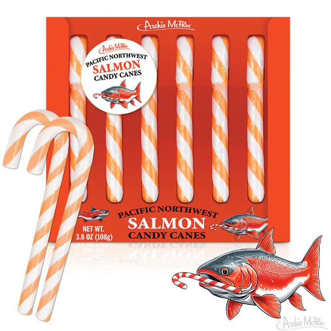 xA box of Pacific Northwest Salmon Candy Canes, featuring orange and white striped candy canes, is displayed alongside an illustration of a salmon. The packaging prominently features the product name and a graphic of the fish.