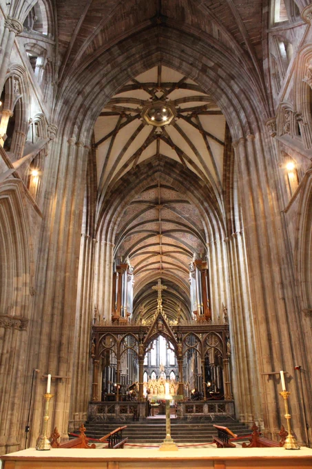 The view shows in the distance the Great East Window. in front of that is the High Altar, which is gilded and the Quire and then the Quire Screen put in by the Victorians. The nave stonework in light brown stone flanks this view leading the eye to the ceiling of the crossing above which is the ringing chamber for the bells.