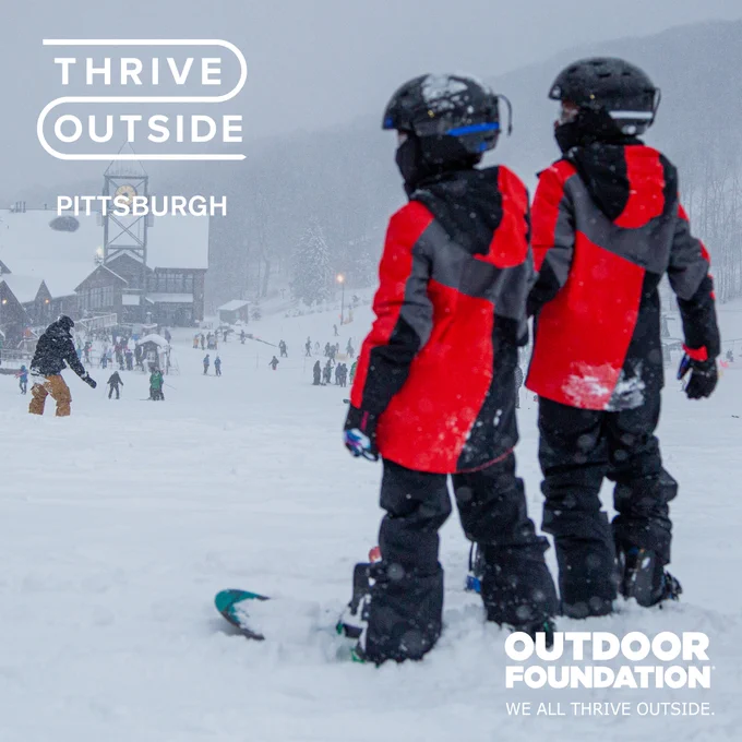 Two individuals in red and black gear standing with snowboards at the base of a snowy hill with other visitors and a large lodge in the background. Text on image includes "Thrive Outside Pittsburgh" and "Outdoor Foundation" logos.