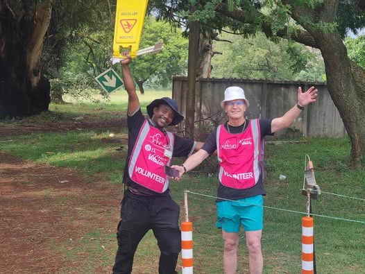 Two parkrun volunteers standing by the finishing line with their arms up.