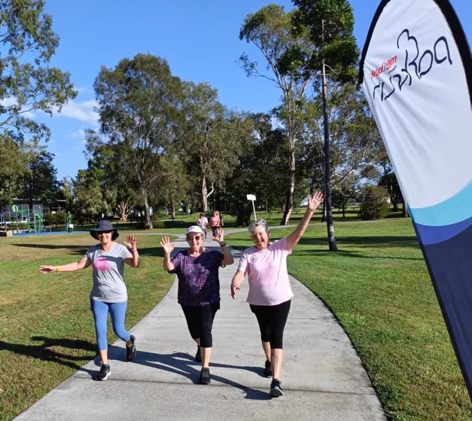 Three parkrunners walking with their arms up on a sunny day.
