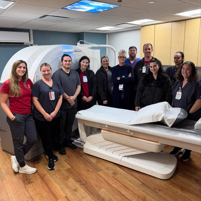 Group of medical staff posing in front of an MRI machine in a hospital.