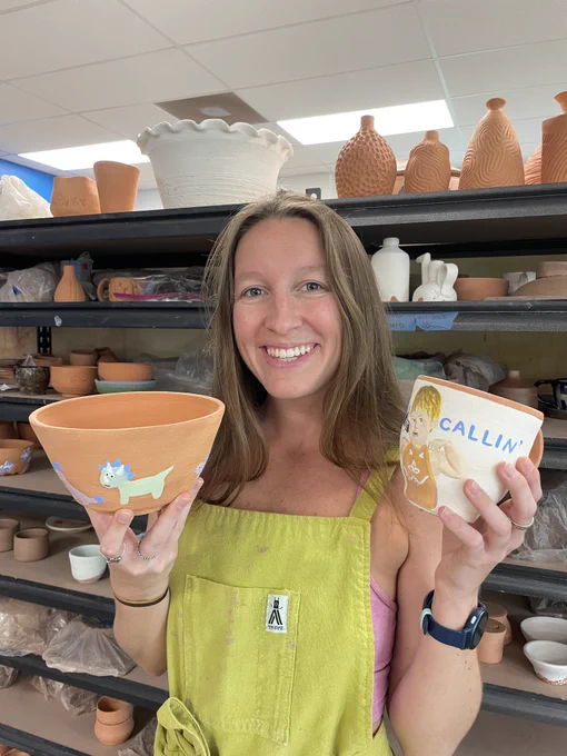 Cali Love wearing a green apron and holding a ceramic bowl and mug.