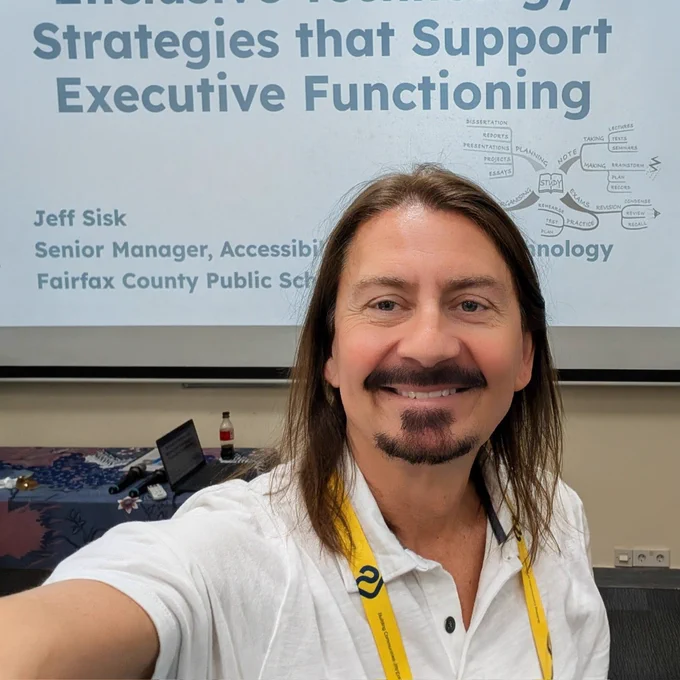 Selfie of Jeff smiling with a presentation screen behind him.