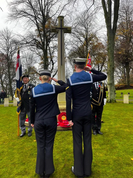 Two sailors stand in their Number One uniform to salute at a war memorial in Pattismuire cemetery, Scotland for Remembrance Day.