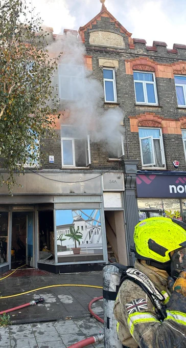 Smoke coming from a first floor window, with a firefighter in the foreground