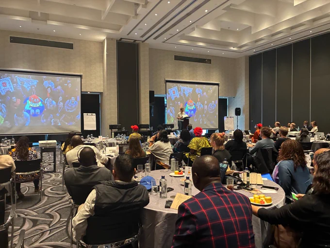 A photo of a room of people sitting at tables looking at a person talking in front of a screen with a "global tax body". 
