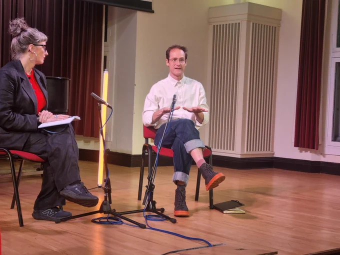 Ali FitzGibbon sits on stage in a Q and A with Anthony Schrag. They are seated with microphones in front of them.