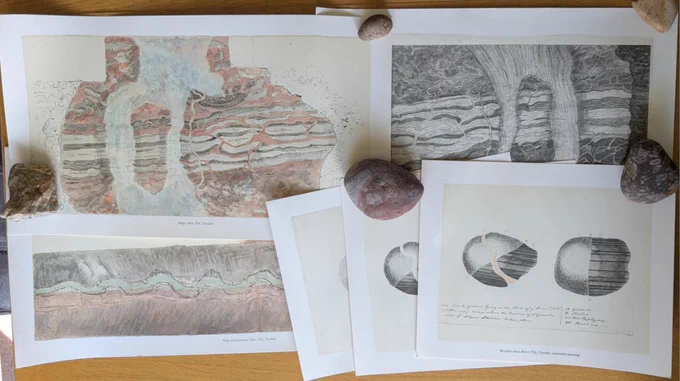 6 prints, three colour sketches and three greyscale lithograph prints, arranged on a wooden table and weighted down with rocks.