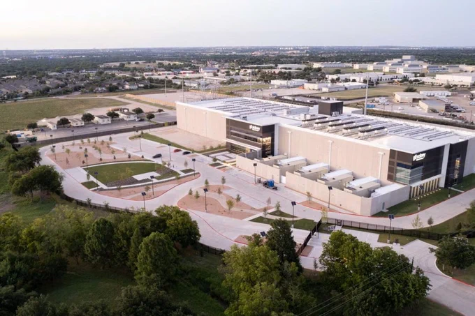 Aerial view of the NVIDIA building complex with surrounding parking areas and landscaped zones, during daylight with a view of the city in the background.