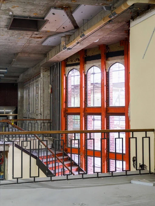 Partially demolished interior space with exposed beams, construction materials, and orange temporary wall framing around a stairwell.