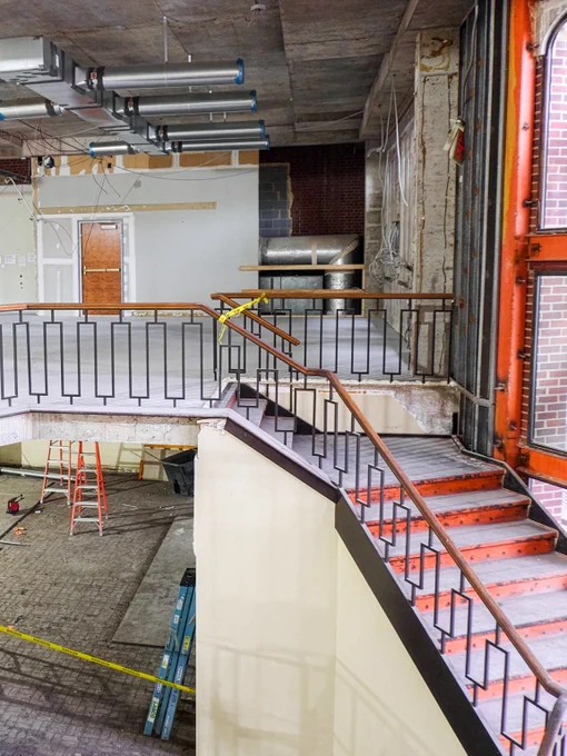 Renovation scene inside the library showing an open multi-level stairwell, scaffolding, ladders, and unfinished walls during construction.