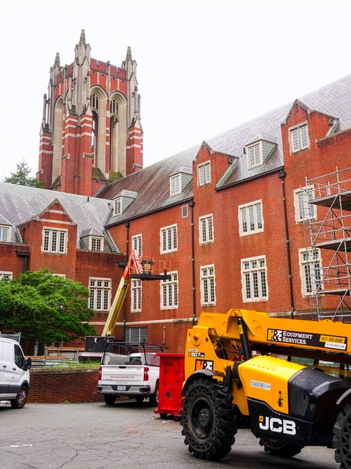 Construction equipment parked outside Boatwright Memorial Library, with a large lift and work materials near the building’s brick tower.