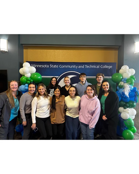 A group of people posing in front of a balloon arch with a sign reading "Minnesota State Community and Technical College."