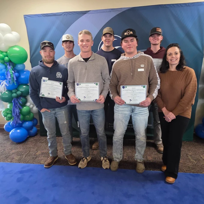 Group of six students and President Brimhall pose with certificates at an academic event, standing in front of a banner with balloons.