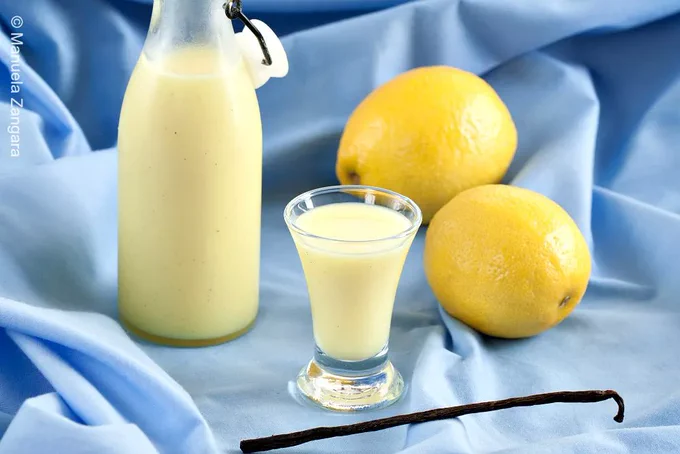 Small glass of Crema di Limoncello beside bottle and fresh lemons.
