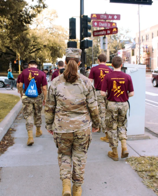 A group of military personnel in camouflage uniforms walking on a sidewalk near the University of Minnesota. 