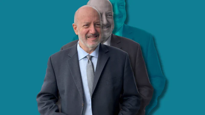 Portrait of Larry Kramer, smiling in a dark suit against a teal background