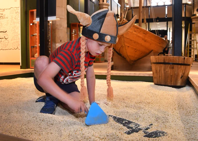 Child in DIG pit wearing a Viking helmet and holding a trowel.