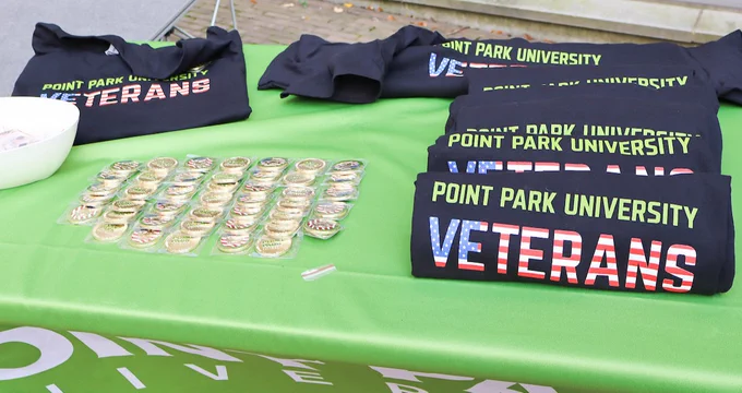 Point Park University Veterans t-shirts and badges, arranged on a green tablecloth.