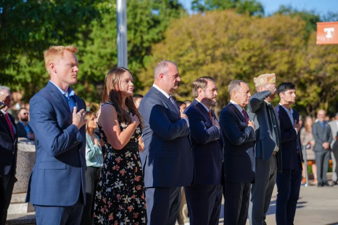 Group of people standing solemnly at an outdoor event.