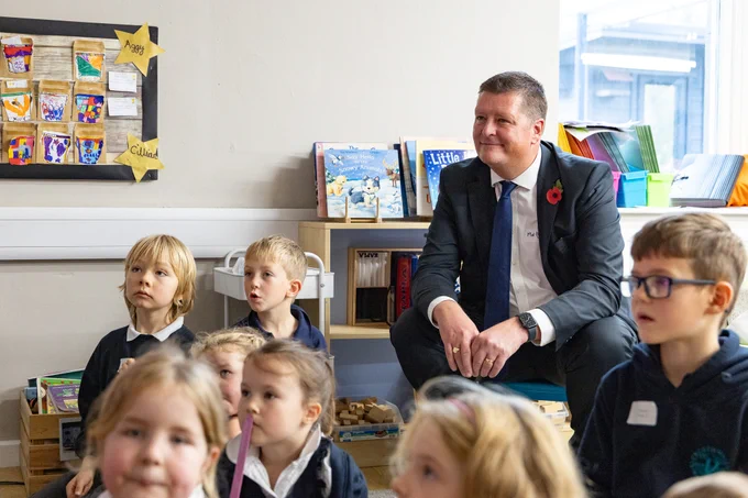 Sir Martyn Oliver sitting behind a group of pupils and observing a lesson at a primary school. 