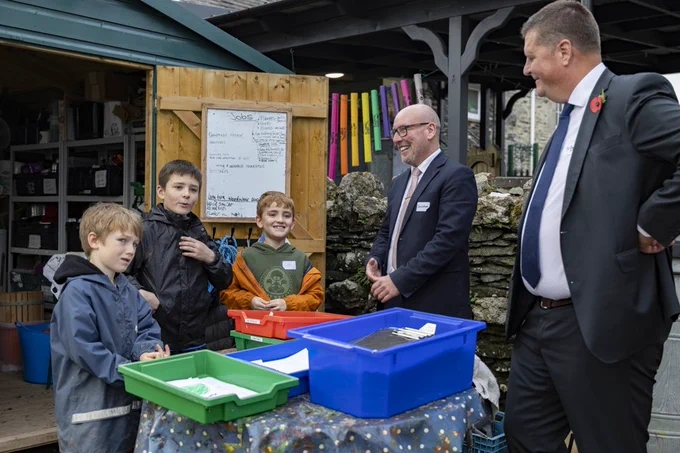 Sir Martyn Oliver and Jonathan Smart talking to three young male pupils outside of a school shed. 