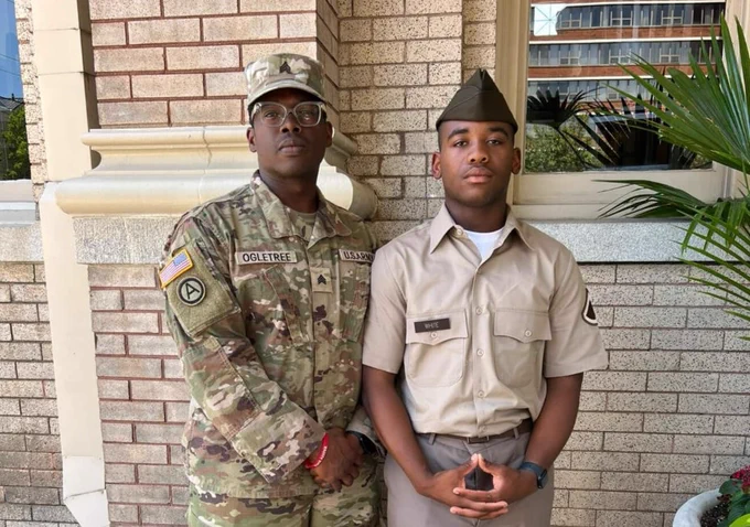 Two military personnel, one in combat uniform and the other in dress uniform, standing side by side in front of a building. The person on the left has a patch that reads "OgilTree" and the person on the right has a name tag labeled "Lewis."