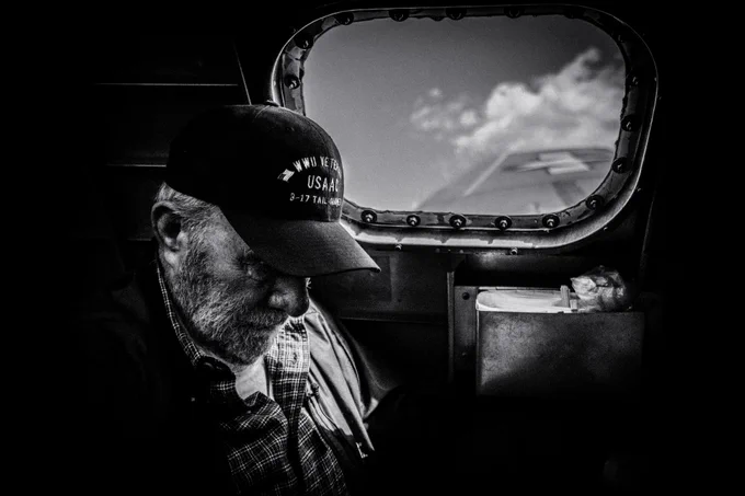 An elderly WWII male veteran is sitting in what appears to be a classic combat plane. He a short white beard and is wearing a Veterans hat with his head down. Photo Source: Eric Ward, Unsplash