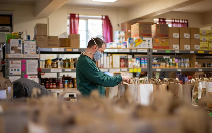 Image of a food bank/ storage area and a man wearing a mask. Unsplash, Aaron  Doucett. 
