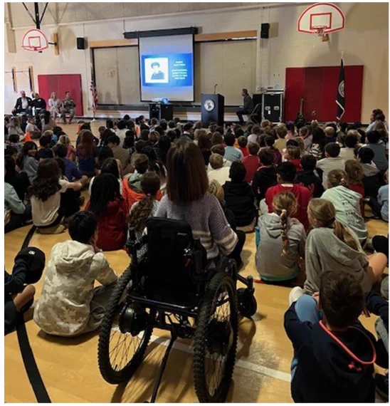 actual view from the back of the gymnasium during a veteran's day assembly. Many students seated in rows