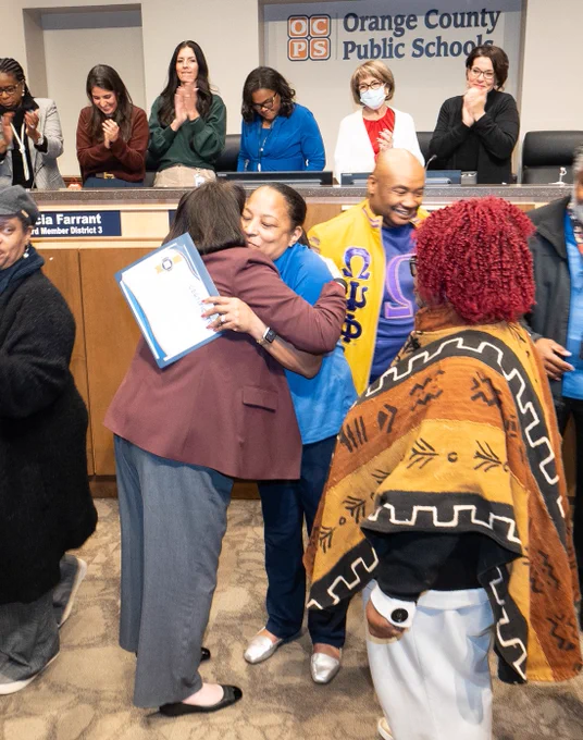 Principal melanie simmons and dr. vazquez hug at school board meeting after simmons is recognized