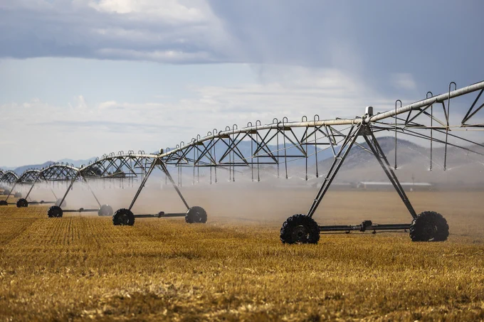 Photograph of pivot irrigation underway over a dry field with virga overhead. Virga is rainfall that evaporates before it reached the surface, leaving visible streaks or rain shafts in the air.  