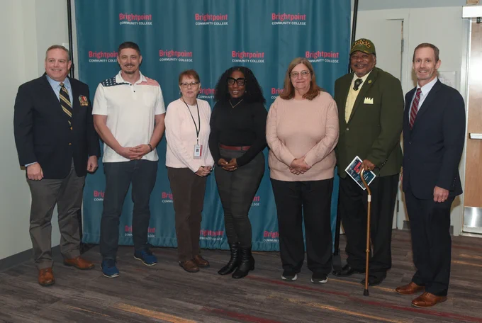 A diverse group of military veterans pose in front of a Brightpoint banner at the 2025 Veterans Day Ceremony. 