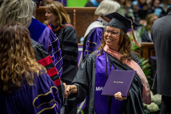 A female graduate of Weber State's Master of Health Administration program shakes hands with faculty members during graduation. 