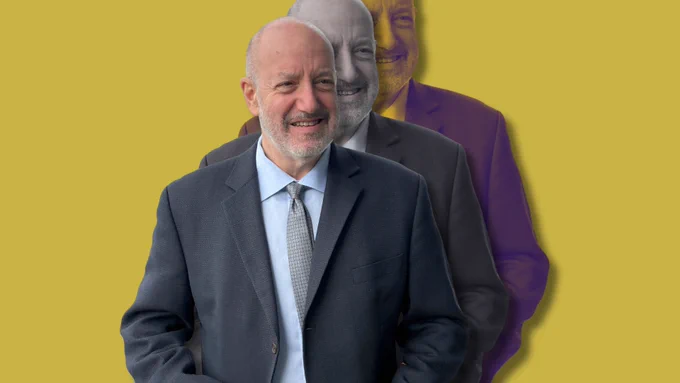 Portrait of Larry Kramer, smiling in a dark suit against a mustard yellow background