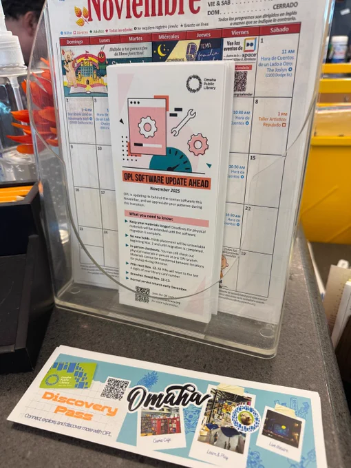 Library desk with a pamphlet and calendar display, and a "Discovery Pass" flyer on the counter.