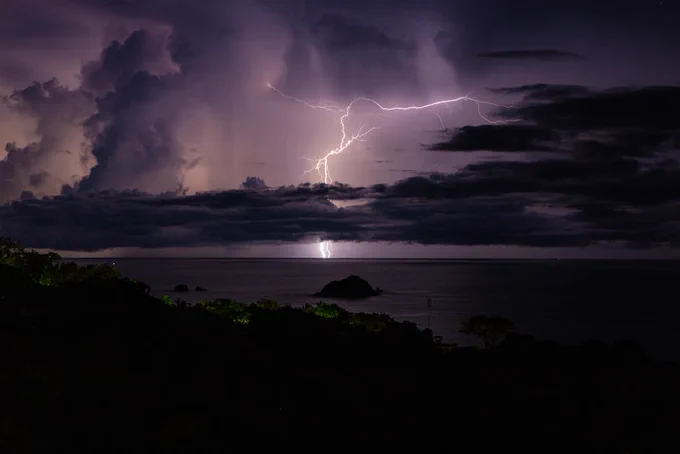 Powerful lightning illuminates a dark ocean scene under dramatic storm clouds.