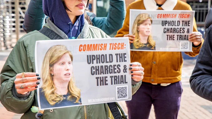 Advocates hold signs reading "Commish Tisch: Uphold the charges and the trial