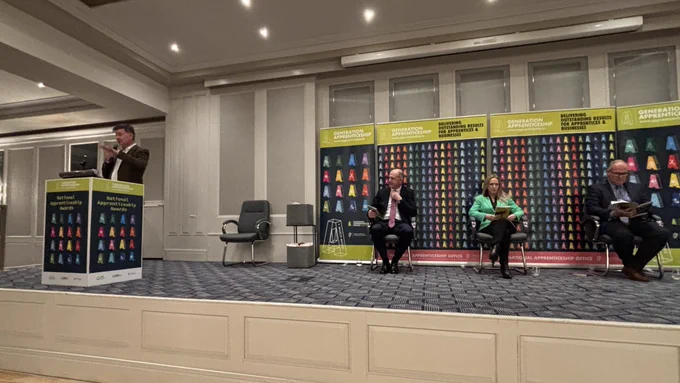 People sitting in a stage with banners behind them.