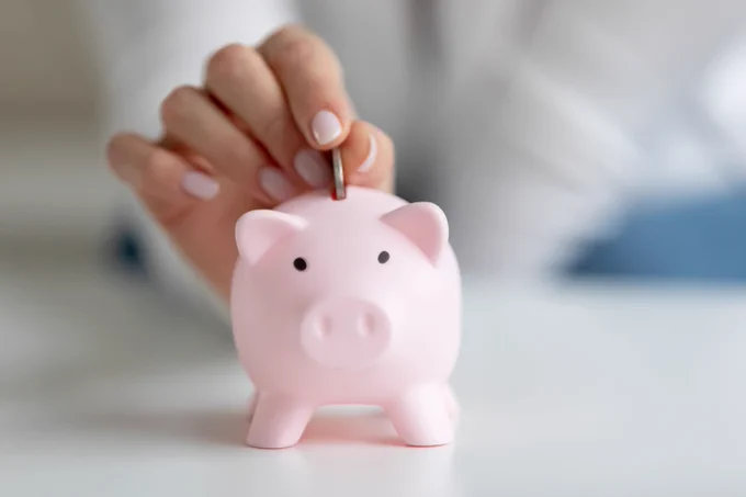A picture of someone putting a coin into a piggy bank