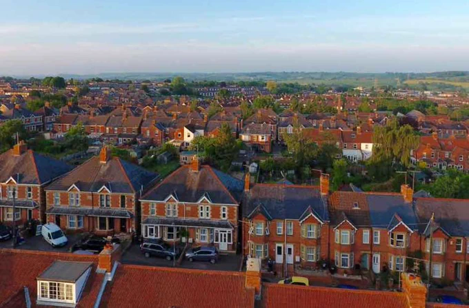 Row of red brick houses with grey tiled rooves and green shrubbery gardens