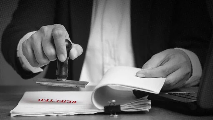 A person stamping a document labeled "REJECTED"