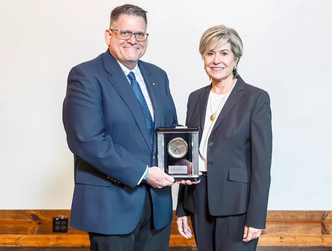 Two individuals smiling and holding an award plaque between them.