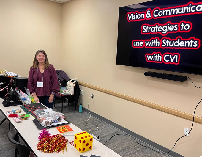 woman standing in front of a table with objects that she has modified for students who have CVI.