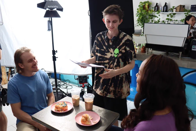 Myself directing two actors seated at a café table with pastries and drinks set in front of them. Everyone is smiling! 