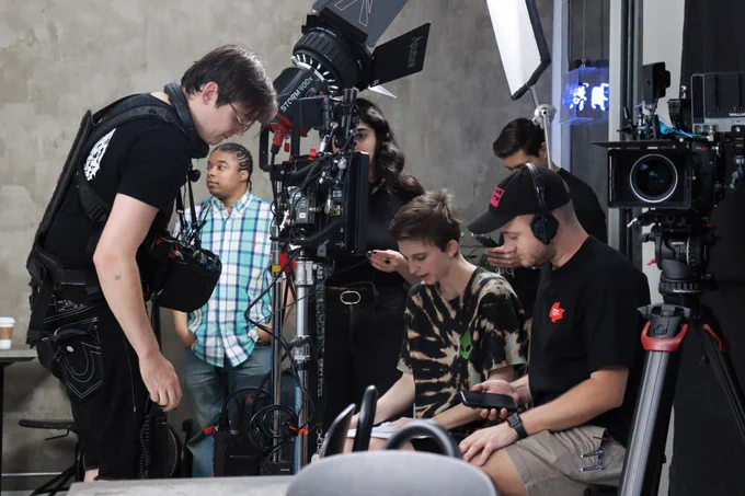 A busy frame with sound, lighting, and camera equipment. All crew members are focused and looking down at a shotlist. 
