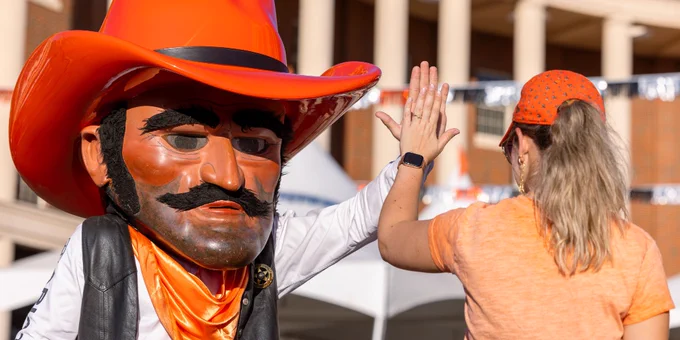 Person giving a high-five to Pistol Pete, the mascot of Oklahoma State University, at an outdoor event.