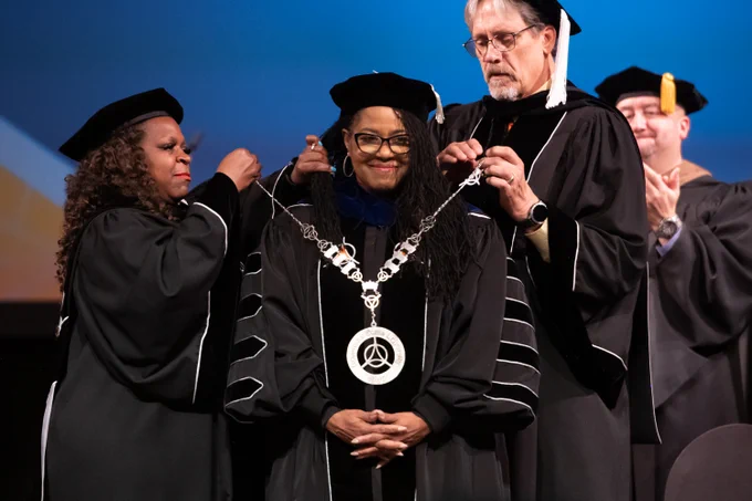 Dr. Ester President of GovState receiving an honorary degree at a university ceremony, flanked by university officials in academic regalia.